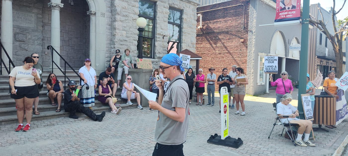 A speaker addresses several dozen residents gathered on the steps of Massena Town Hall